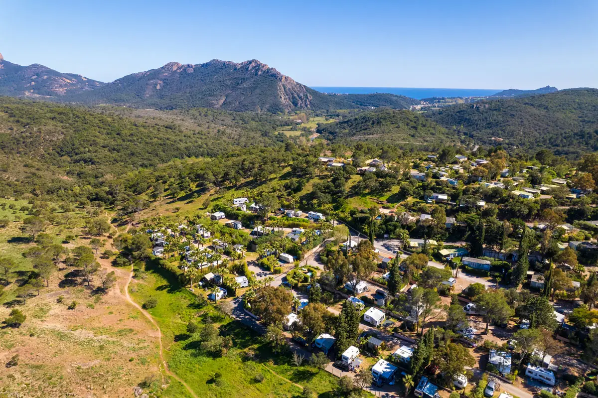 Vue aérienne du domaine d'Esterel Caravaning à Agay, ses emplacements sous les pins, le massif de l'Estérel et la mer à l'horizon