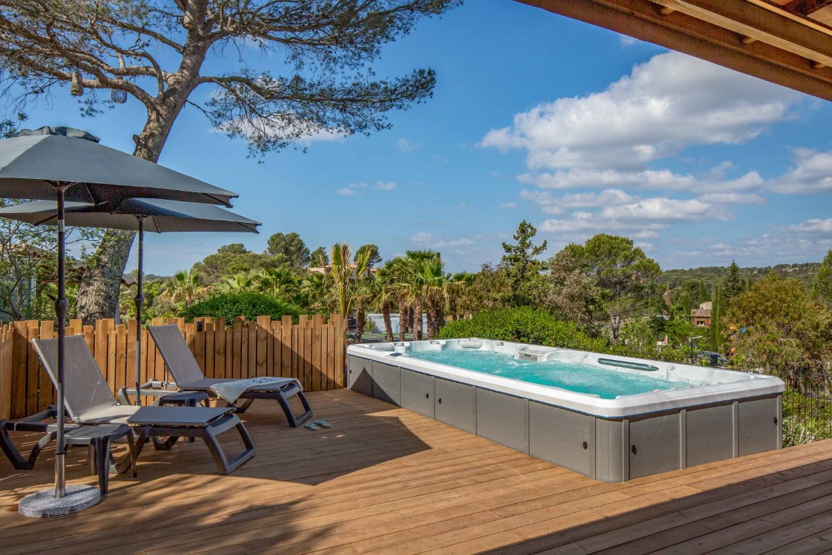 Spa de nage privé et transats sur la terrasse en bois du VIP Duo d'Esterel Caravaning, sous les pins
