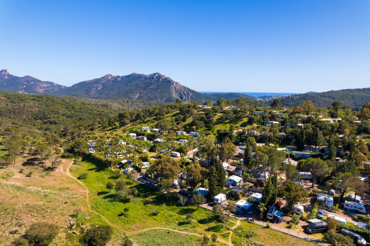 Vue aérienne d'Esterel Caravaning à Agay, ses emplacements dans la verdure et le massif de l'Estérel au loin