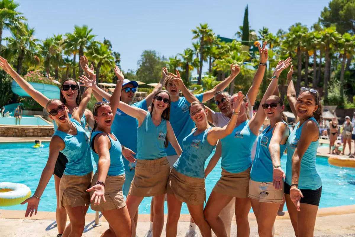 L'équipe d'Esterel Caravaning, bras levés et tout sourire, au bord de la piscine sous les palmiers