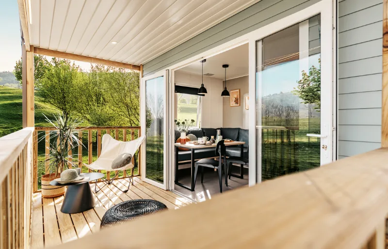 Terrasse couverte du mobil-home Villa avec salon de jardin et baie vitrée ouverte sur l'espace repas